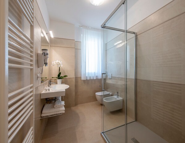 Un baño moderno con cabina de ducha de vidrio, un lavamanos blanco y un bidé.