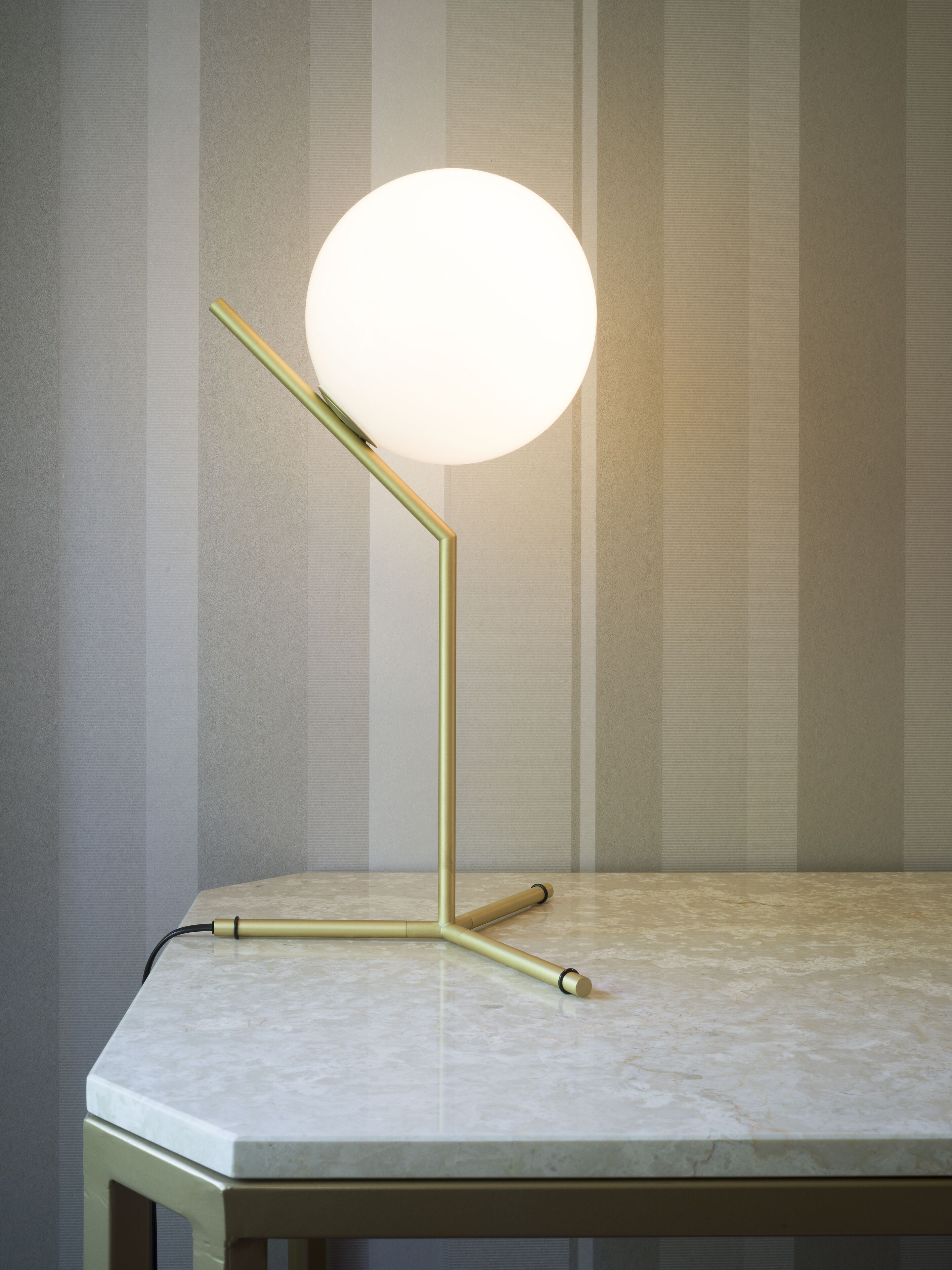 A modern floor lamp with a spherical light fixture on a marble-topped table against a striped wallpaper background.