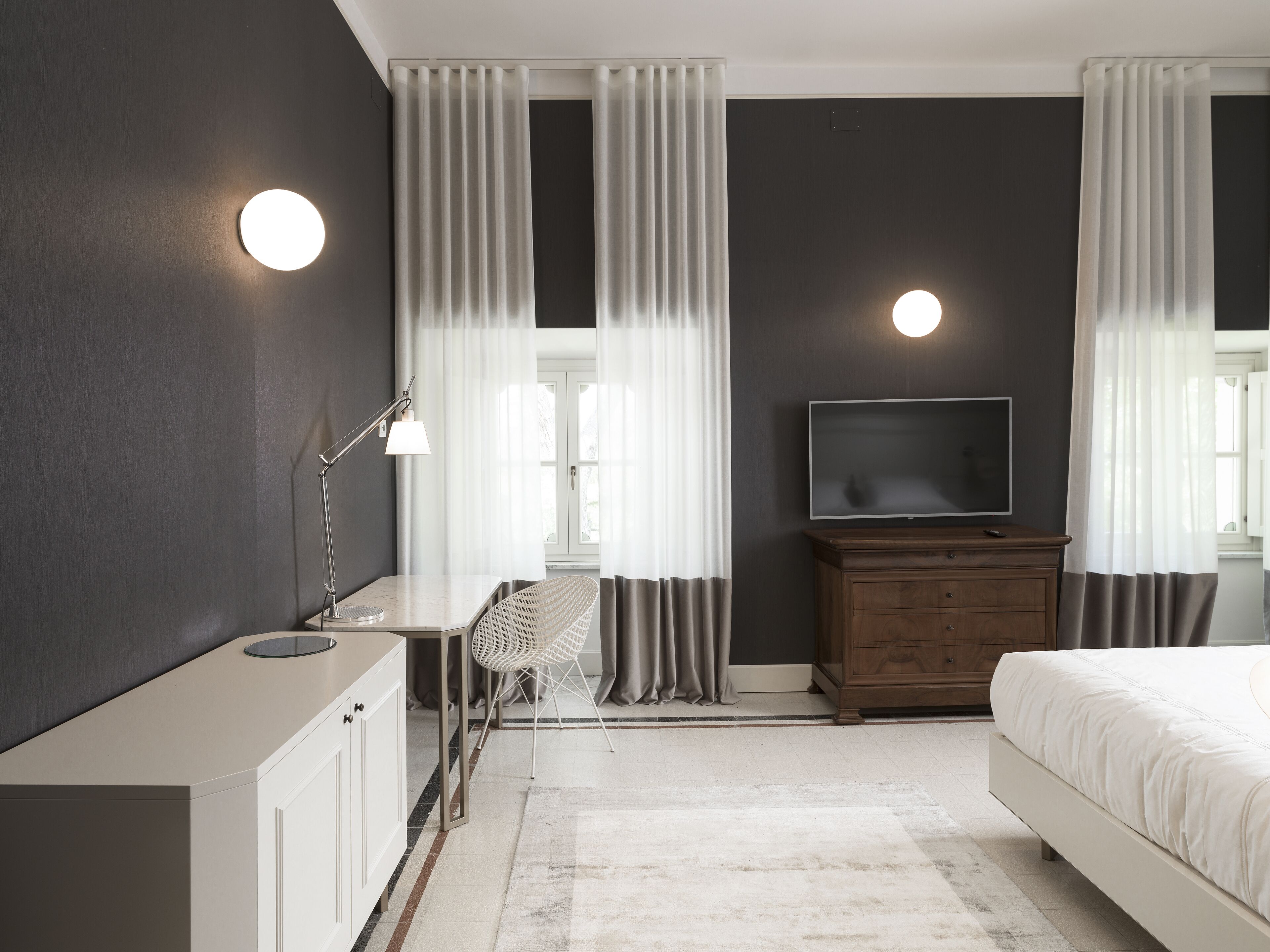 Een moderne slaapkamer met een bed, televisie, nachtkastje, lamp en gordijnen.