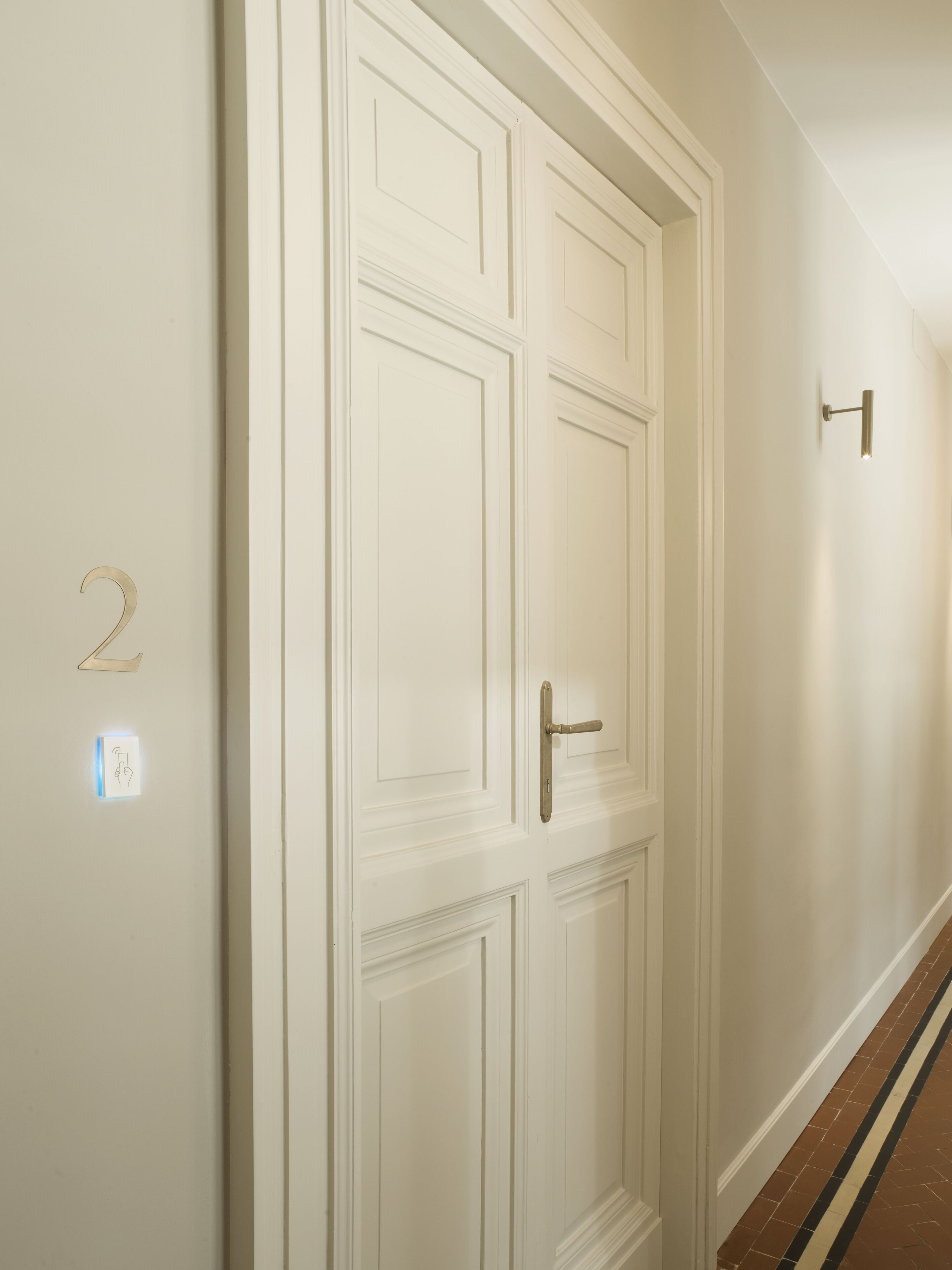 A hallway with a white door, a wall-mounted light fixture, and a number '2' sign.