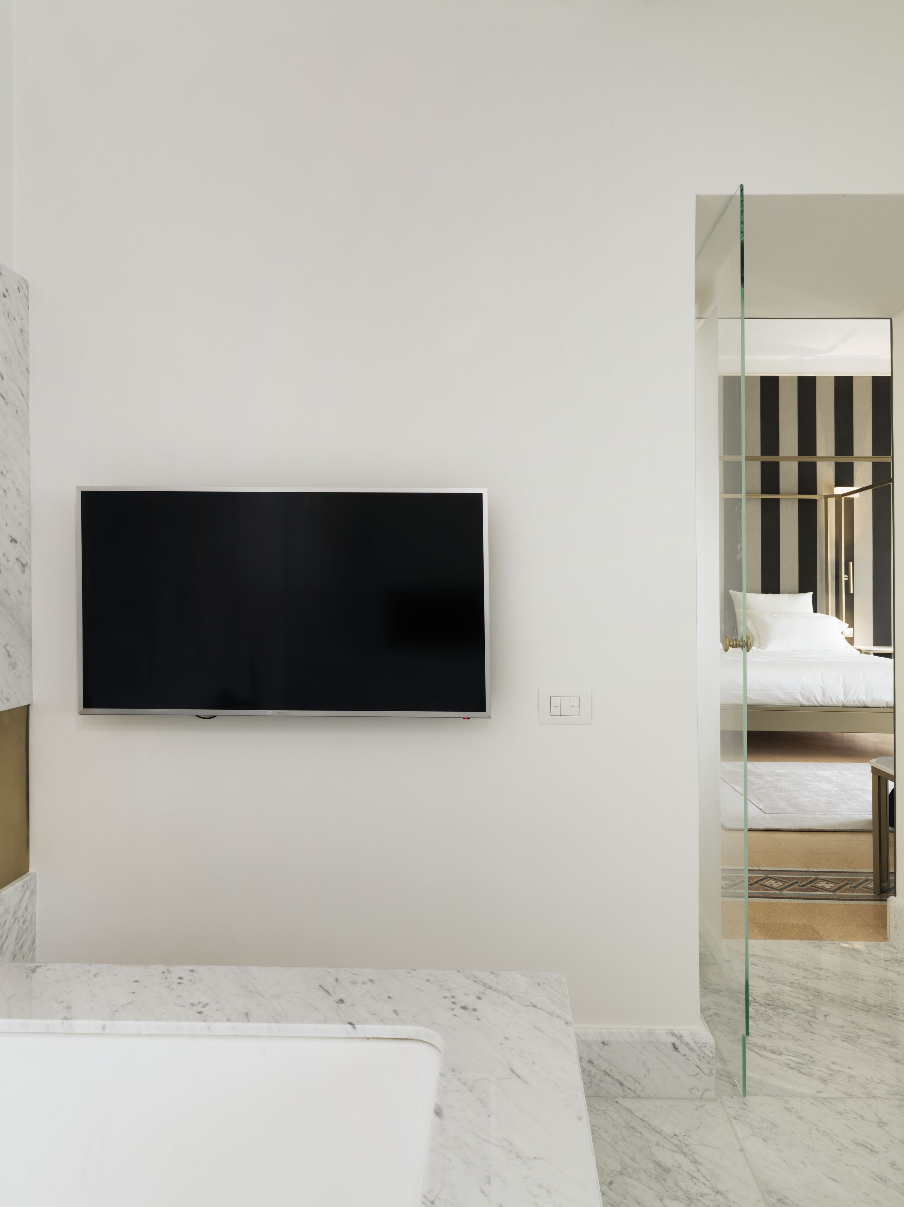 A modern bathroom with a large mirror, a marble countertop, and a mounted television.