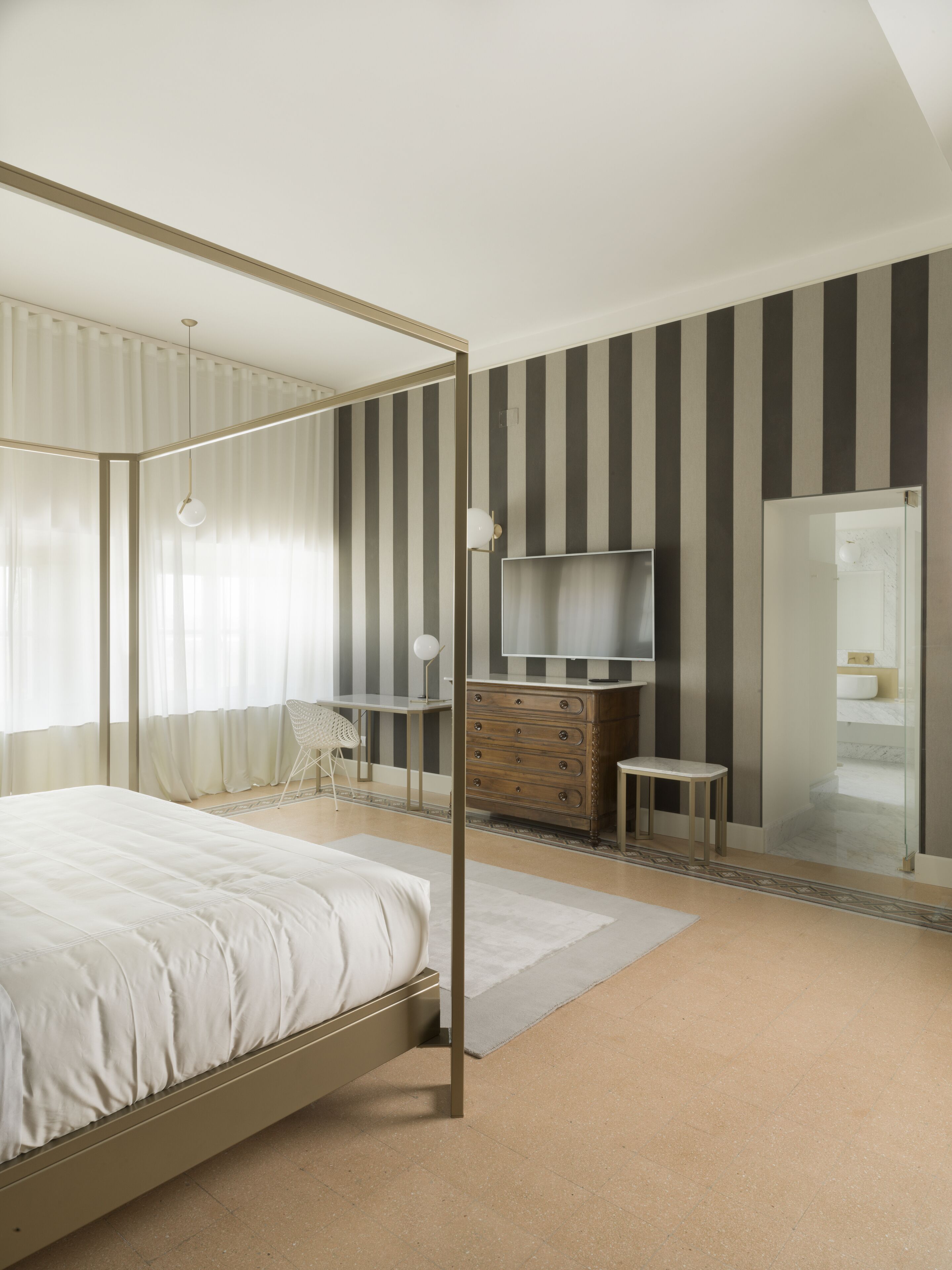 Un dormitorio con cama con dosel, un escritorio con silla, cómoda, televisor y espejo.