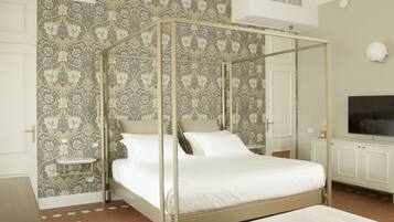Ein Bett mit Baldachin, eine weiße Matratze und Kissen, ein Nachttisch, ein Fernseher, ein Schrank und eine Wand mit Musterung.