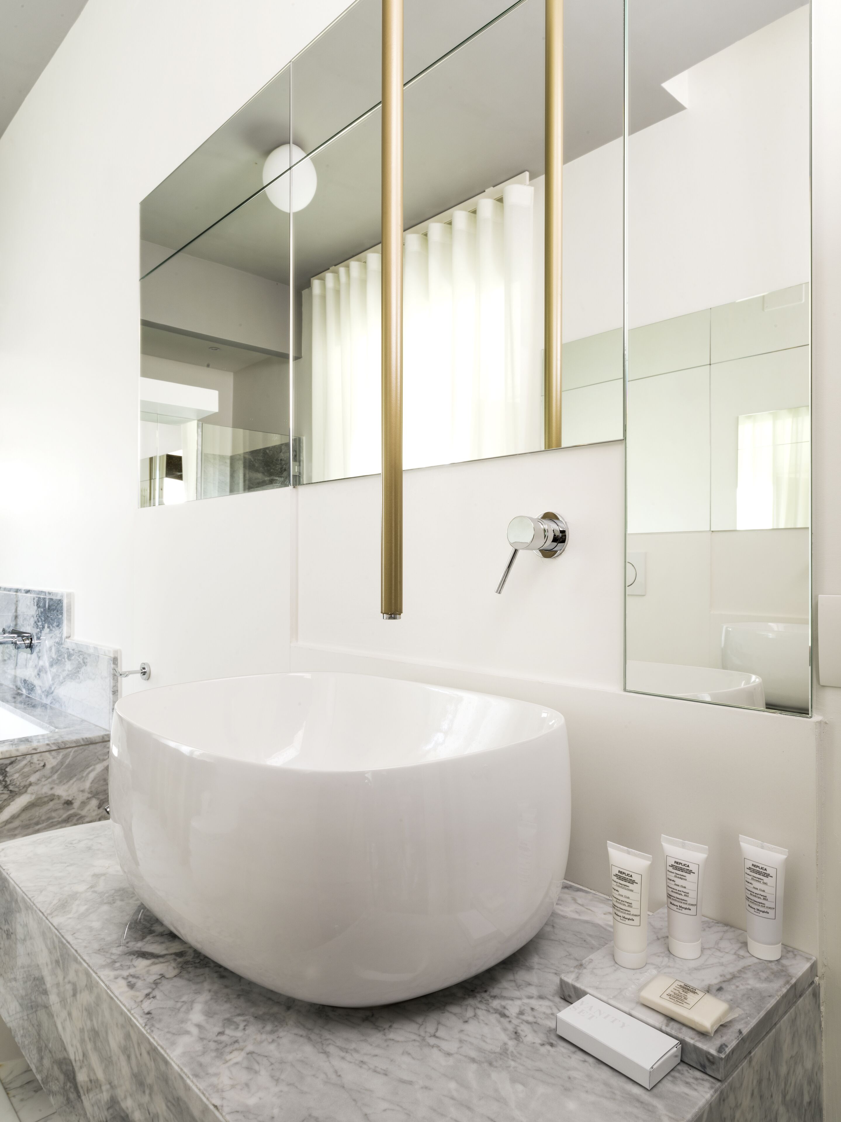 A modern bathroom with a large oval sink, marble countertops, and a large mirror with gold accents.