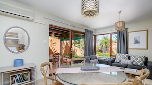 A modern living room with a glass-top dining table, wooden chairs, a sofa with patterned cushions, a bookshelf, and a large mirror. - San Lameer Villa Rentals 2007 (Southbroom)