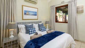 A neatly made bed with a blue blanket, two bedside lamps, and a framed picture on the wall. - San Lameer Villa Rentals 2007 (Southbroom)