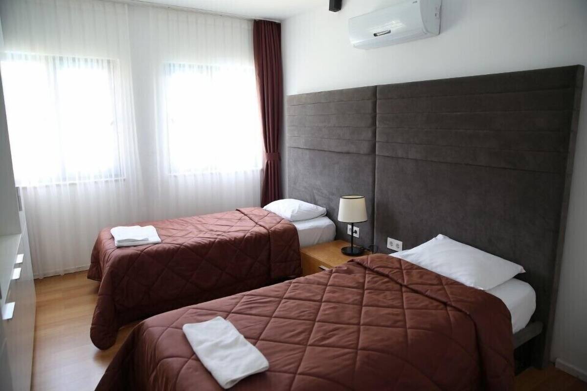 Ein Hotelzimmer mit zwei Betten, einem Nachttisch mit Lampe und einem Fenster mit Vorhängen.