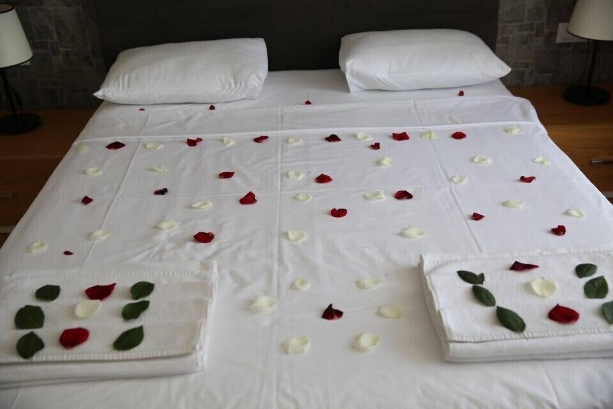 Ein ordentlich gemachtes Bett mit weißen Leinen und verstreuten Rosenblüten.