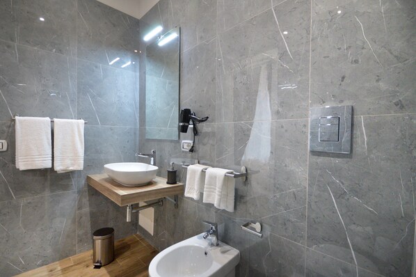 Et moderne badeværelse med et stort spejl, en skålhåndvask, et bidet og en træbordplade.