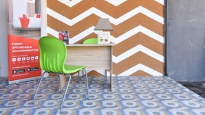 A hotel reception area with a chevron-patterned wall, a green chair, a desk with a lamp, and a RedDoorz advertisement.