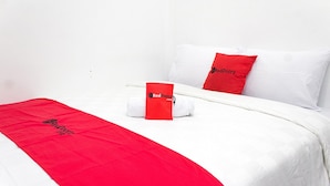 A hotel room with a neatly made bed, a red blanket, and a red pillow with the hotel's logo. - RedDoorz @ Galuh Mas (Karawang)