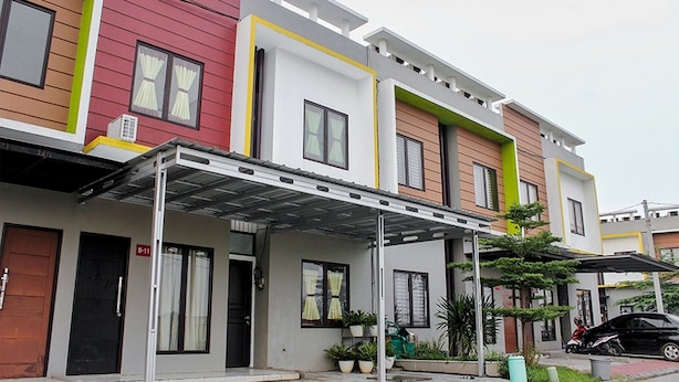 A row of modern multi-story residential buildings with a covered entrance area, potted plants, and a parked motorcycle. - RedDoorz @ Galuh Mas (Karawang)