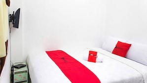 A hotel room with a bed, a red throw, a pillow with a logo, a small table with a red item, and a wall-mounted TV. - RedDoorz @ Galuh Mas (Karawang)