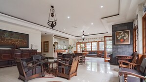 A spacious living room with a large wooden coffee table, several wooden chairs, a chandelier, and a painting on the wall.
