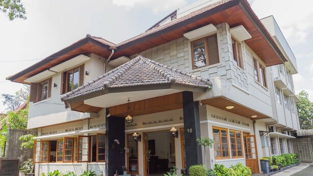 A two-story building with a tiled roof, large windows, and a covered entrance area with potted plants.