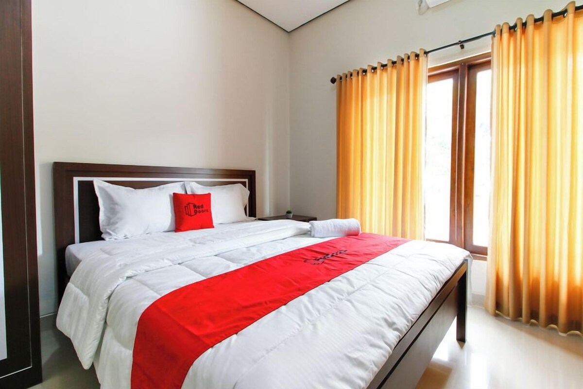 A hotel room with a bed, a red pillow, and curtains.