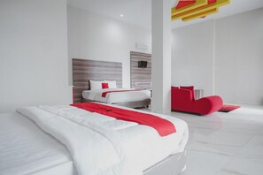 A modern hotel room with a large bed, a red accent wall, and a minimalist design.