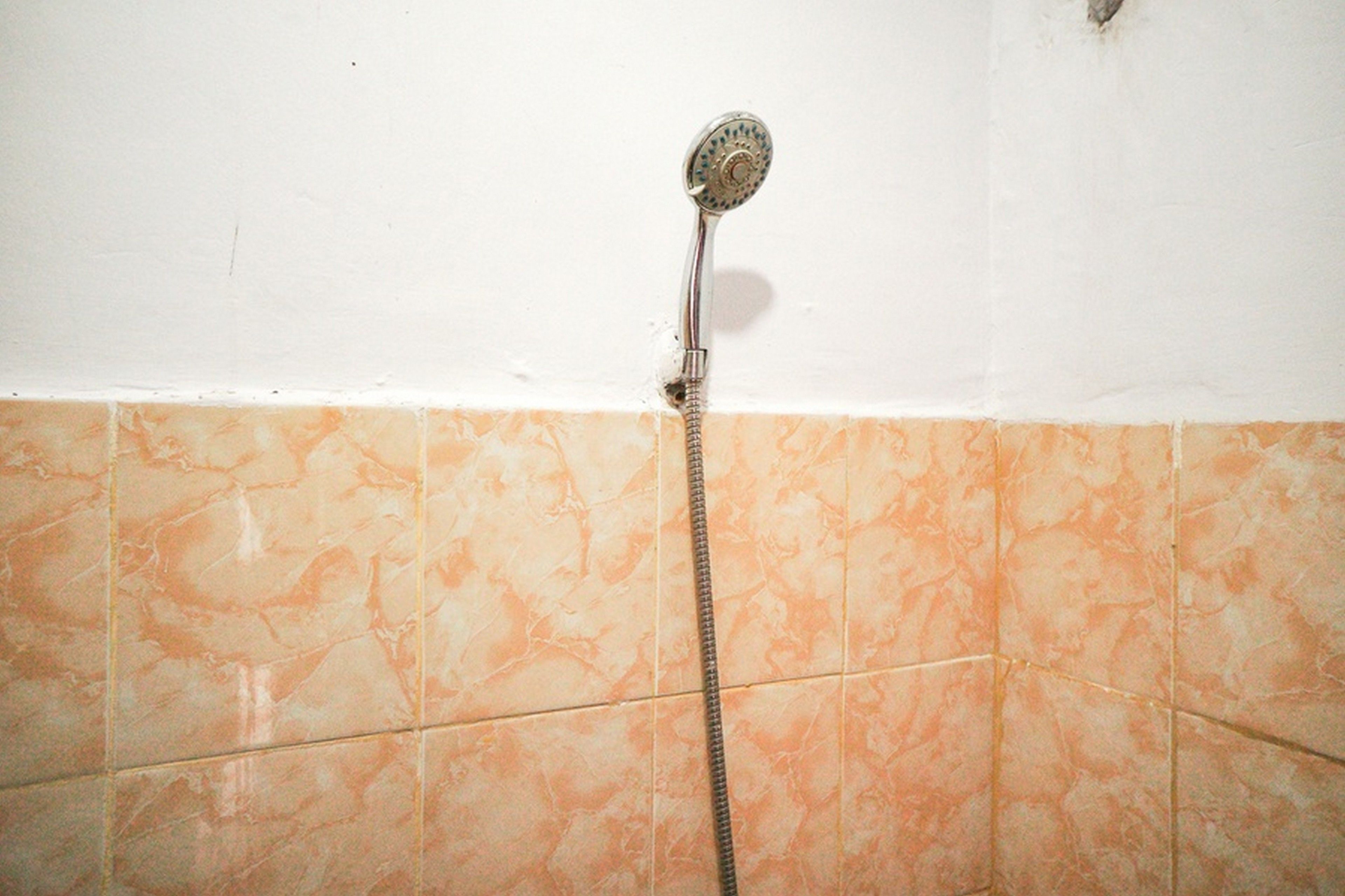 A shower with a handheld showerhead and a hose, set against a tiled wall with a marble-like pattern.