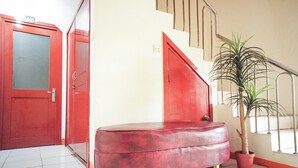 A red bench in a hallway with a potted plant and a red door. - RedDoorz near Palembang Square Mall 2 (Palembang)