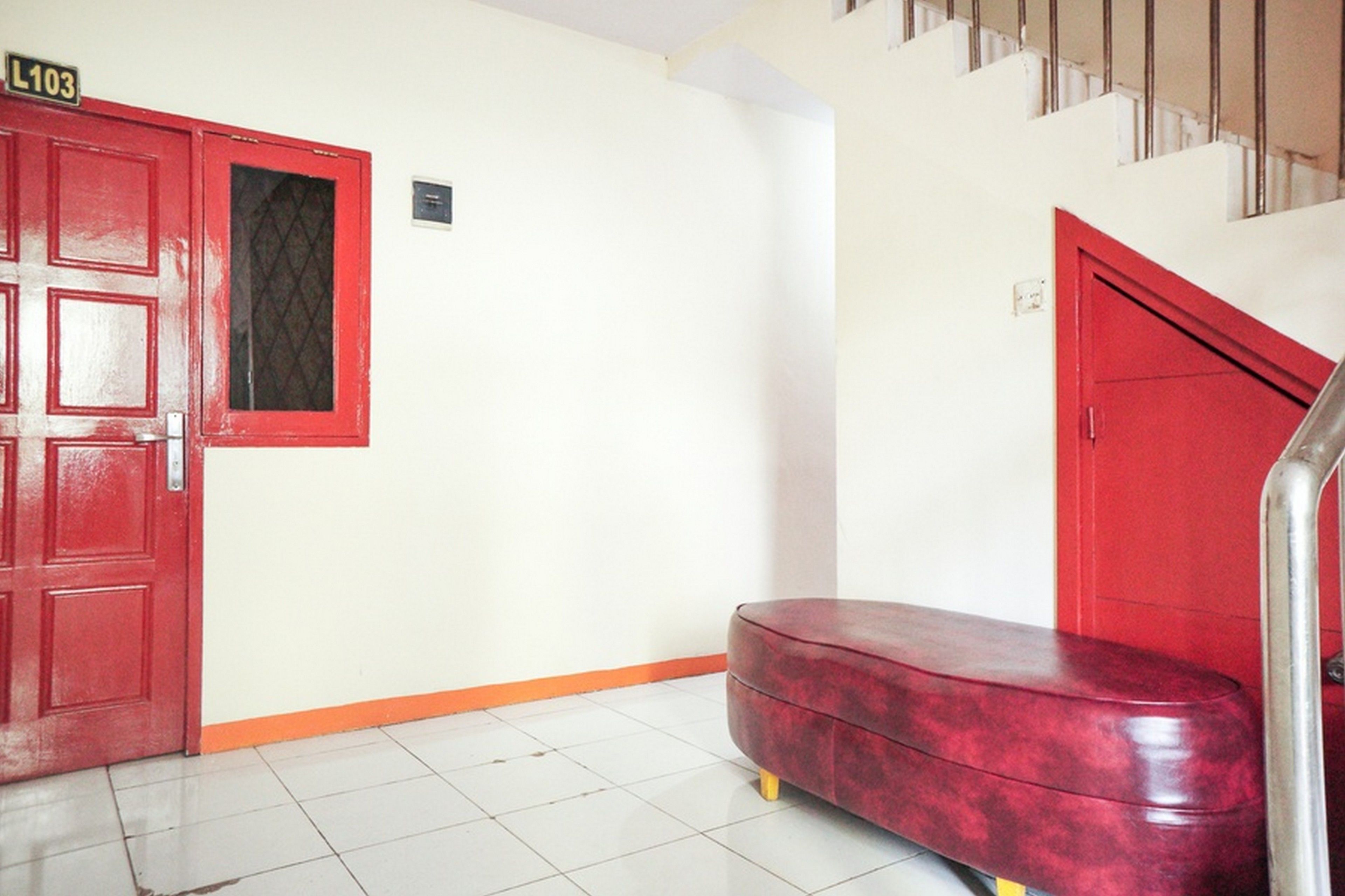 Una puerta roja con un letrero que dice "L103", un banco rojo y una escalera con barandillas metálicas.