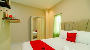 A hotel room with a bed, a red and white bedspread, a red pillow, a green curtain, and a wardrobe. - RedDoorz Syariah @ Panglima Polem Aceh (Banda Aceh)