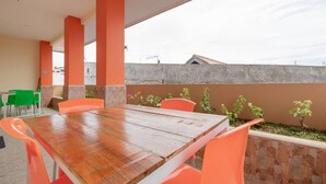 An outdoor dining area with a wooden table and orange chairs, surrounded by a low stone wall and small plants. - RedDoorz Syariah @ Panglima Polem Aceh (Banda Aceh)