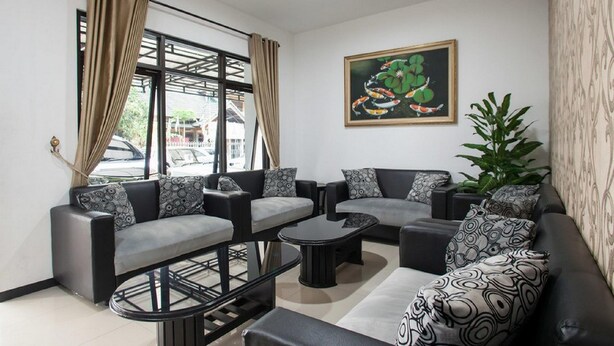A modern living room with a sofa set, a coffee table, and a dining table. There is a painting on the wall and a plant on the right side.