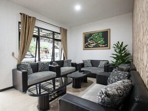 A modern living room with a sofa set, a coffee table, and a dining table. There is a painting on the wall and a plant on the right side. - RedDoorz near Taman Krida Budaya Malang (Malang)