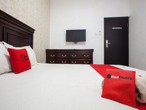 A hotel room with a bed, a television mounted on the wall, a dark wooden dresser, and a door with a handle. - RedDoorz near Taman Krida Budaya Malang (Malang)