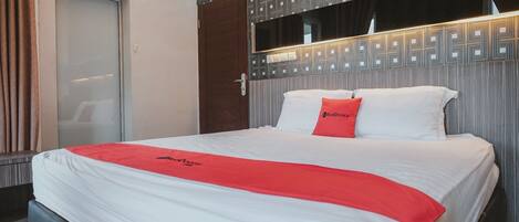 Una habitación de hotel con cama, una manta roja y un cabecero de estampado geométrico.