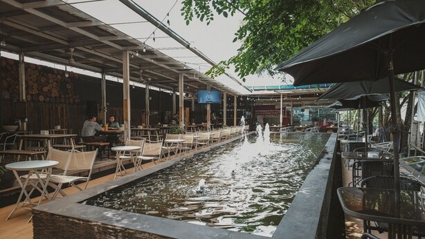 An outdoor dining area with tables and chairs, a water feature, and a covered seating area. - RedDoorz @ Jamin Ginting Medan (Medan)