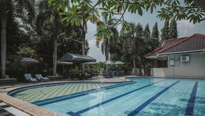 A swimming pool with a checkered pattern, surrounded by lounge chairs and umbrellas, with palm trees and a building in the background. - RedDoorz @ Jamin Ginting Medan (Medan)