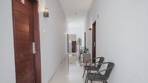 A hallway with a wooden door, metal chairs, and a plant. - RedDoorz @ Jamin Ginting Medan (Medan)