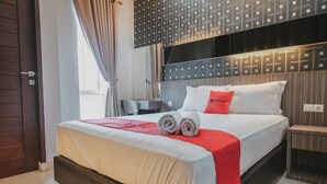 A modern hotel room with a large bed, a red accent pillow, and a neatly made bed with rolled towels. - RedDoorz @ Jamin Ginting Medan (Medan)