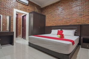 A hotel room with a brick wall, a large bed with white bedding and red accents, a wooden wardrobe, a desk, and a mirror. - RedDoorz Plus near Cambridge City Square 2 (Medan)