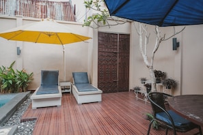 Une terrasse avec deux chaises longues, un parasol jaune, une table à manger et des plantes en pot.