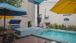 Ein Außenpoolbereich mit Liegestühlen und Sonnenschirmen, umgeben von einem Gebäude mit Kachelfassade.