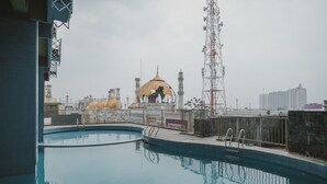 A swimming pool with a view of a mosque and surrounding buildings. - RedDoorz Apartment @ Saladin Mansion Margonda (Depok)
