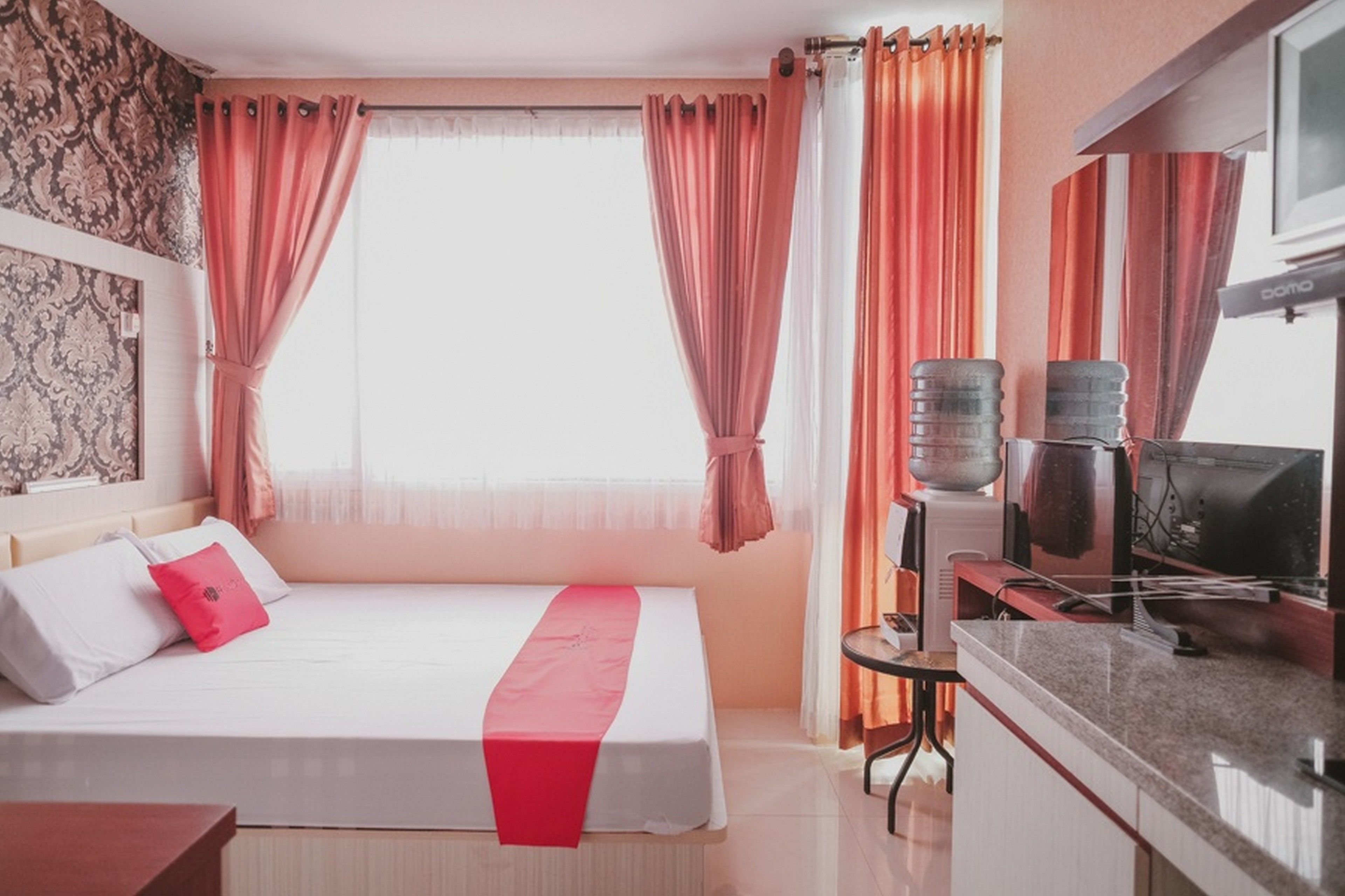 A hotel room with a bed, a desk, a television, and a window with curtains.