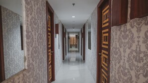 A corridor with patterned wallpaper and wooden doors, leading to a room with a tiled floor. - RedDoorz Apartment @ Saladin Mansion Margonda (Depok)