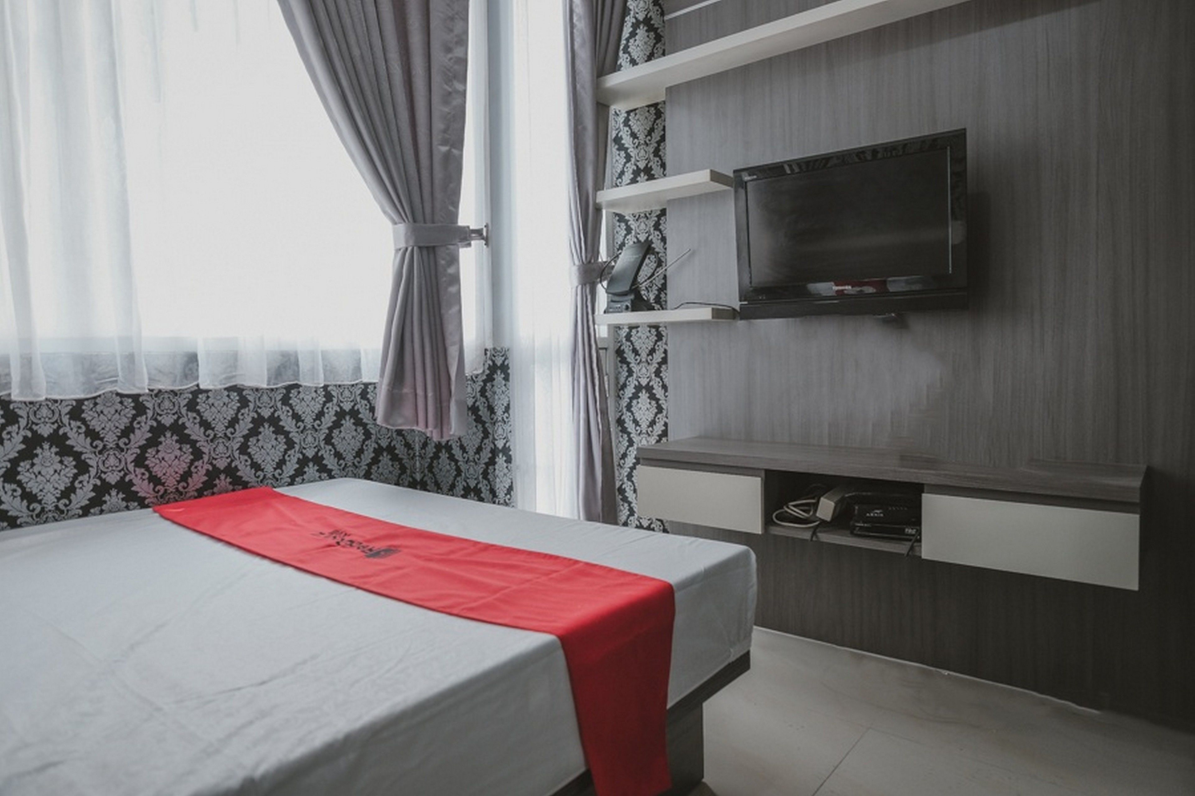 A hotel room with a bed, a TV mounted on the wall, and a desk with a chair.