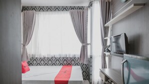 A hotel room with a bed, a TV, and a window with curtains. - RedDoorz Apartment @ Saladin Mansion Margonda (Depok)
