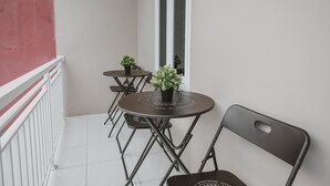 Een balkon met een witte railing, twee kleine ronde tafels met potplanten, en een enkele stoel.