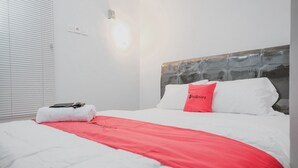 Een net opgemaakt bed met wit- en rood beddengoed, een rood kussen en een witte handdoek ernaast.
