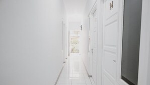 Een lichte, witte gang met deuren aan de rechterkant, leidend naar een balkon met uitzicht.