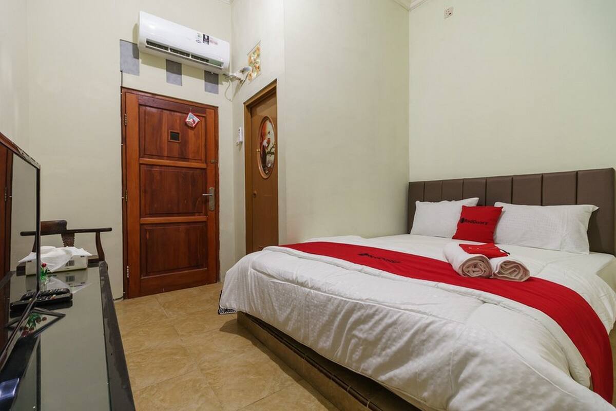 A hotel room with a bed, a desk with a computer, and a door.