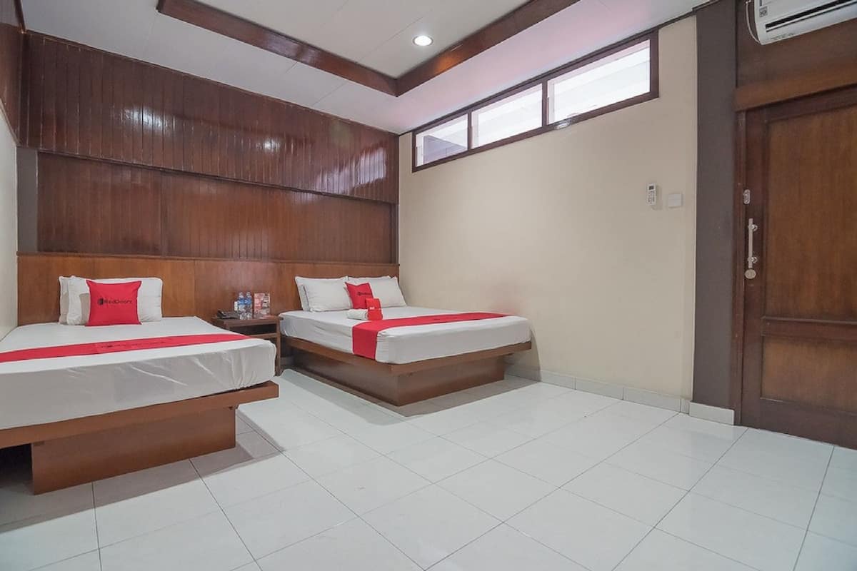 A hotel room with two beds, wooden headboards, white bedding, and a window providing natural light.