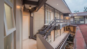 Un edificio moderno con una escalera que lleva a un nivel superior, ventanas amplias y un pequeño espacio exterior con una jardinera.