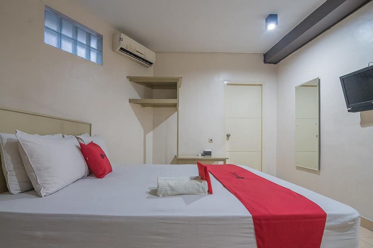 A hotel room with a bed, a small table, a TV, and a window.