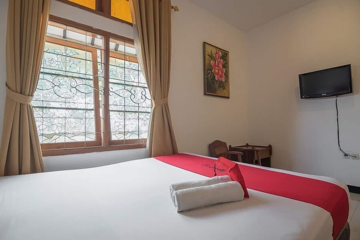 A hotel room with a bed, a television, a desk, and a window with curtains.